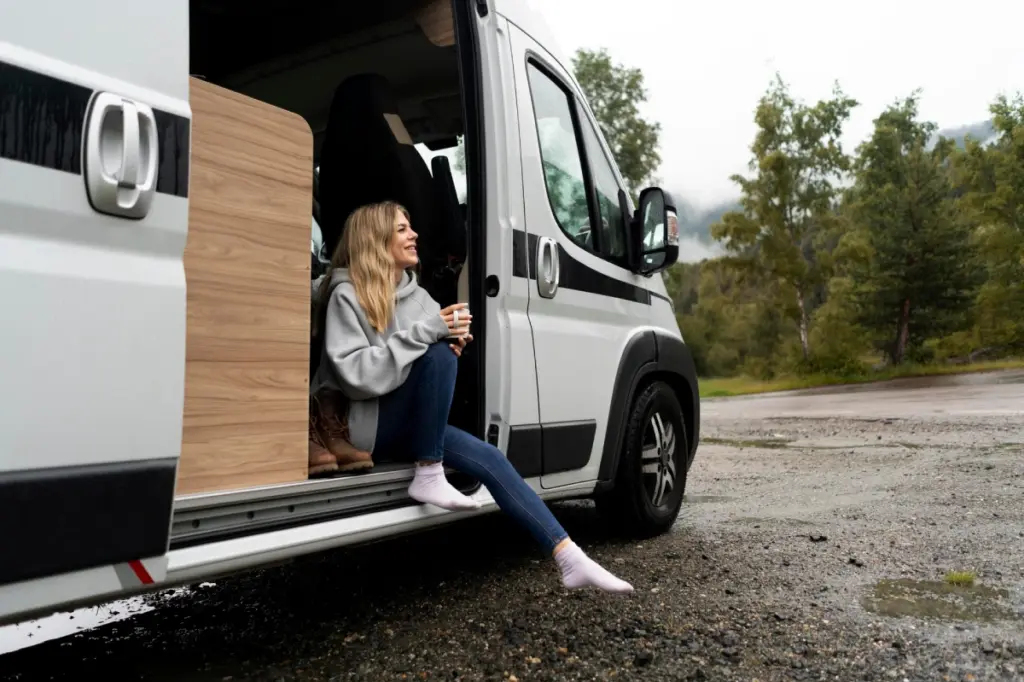 mujer sentada en furgoneta camperizada bebiendo